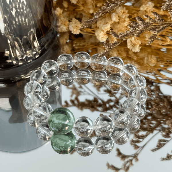 Clear Quartz bracelet with green crystal bead on reflective surface