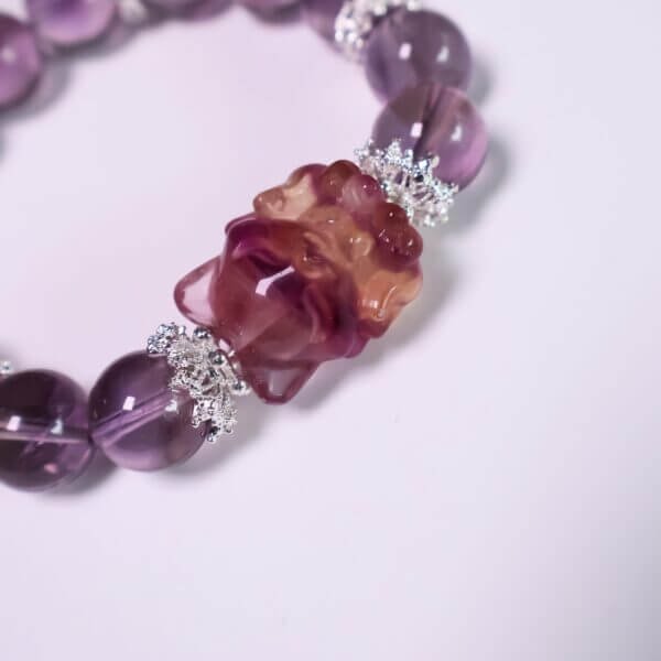 Purple amethyst bracelet displayed on a reflective surface with floral decor.