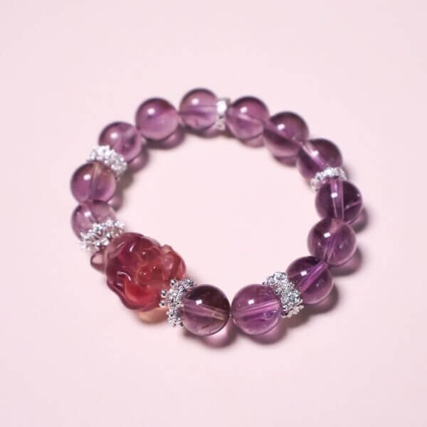 Purple amethyst bracelet displayed on a reflective surface with floral decor.